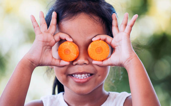 Chica sosteniendo rodajas de zanahoria sobre sus ojos y sonriendo