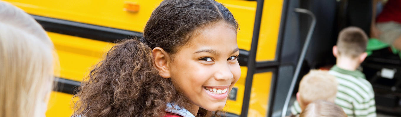 Estudiante sonriendo frente al autobús escolar