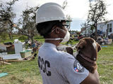 AmeriCorps - joven sosteniendo un perro mientras mira el área de desastre de la tormenta