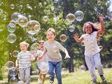Children running outside through soap bubbles in a park
